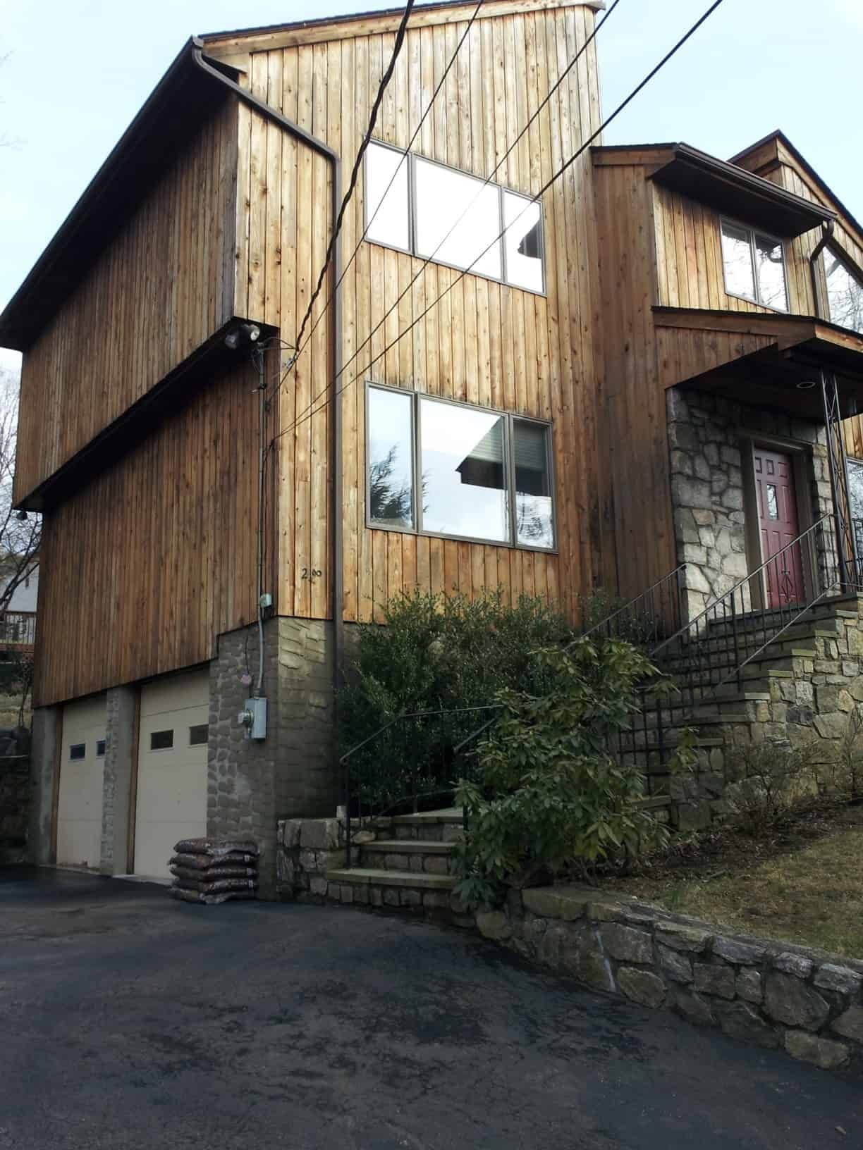 Two-story wood-sided house with a stone foundation and steps leading up to the front door, with a two-car garage.