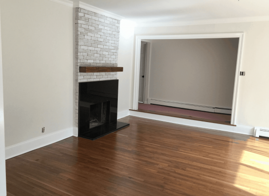 Empty living room with fireplace and doorway to another room; hardwood floors.