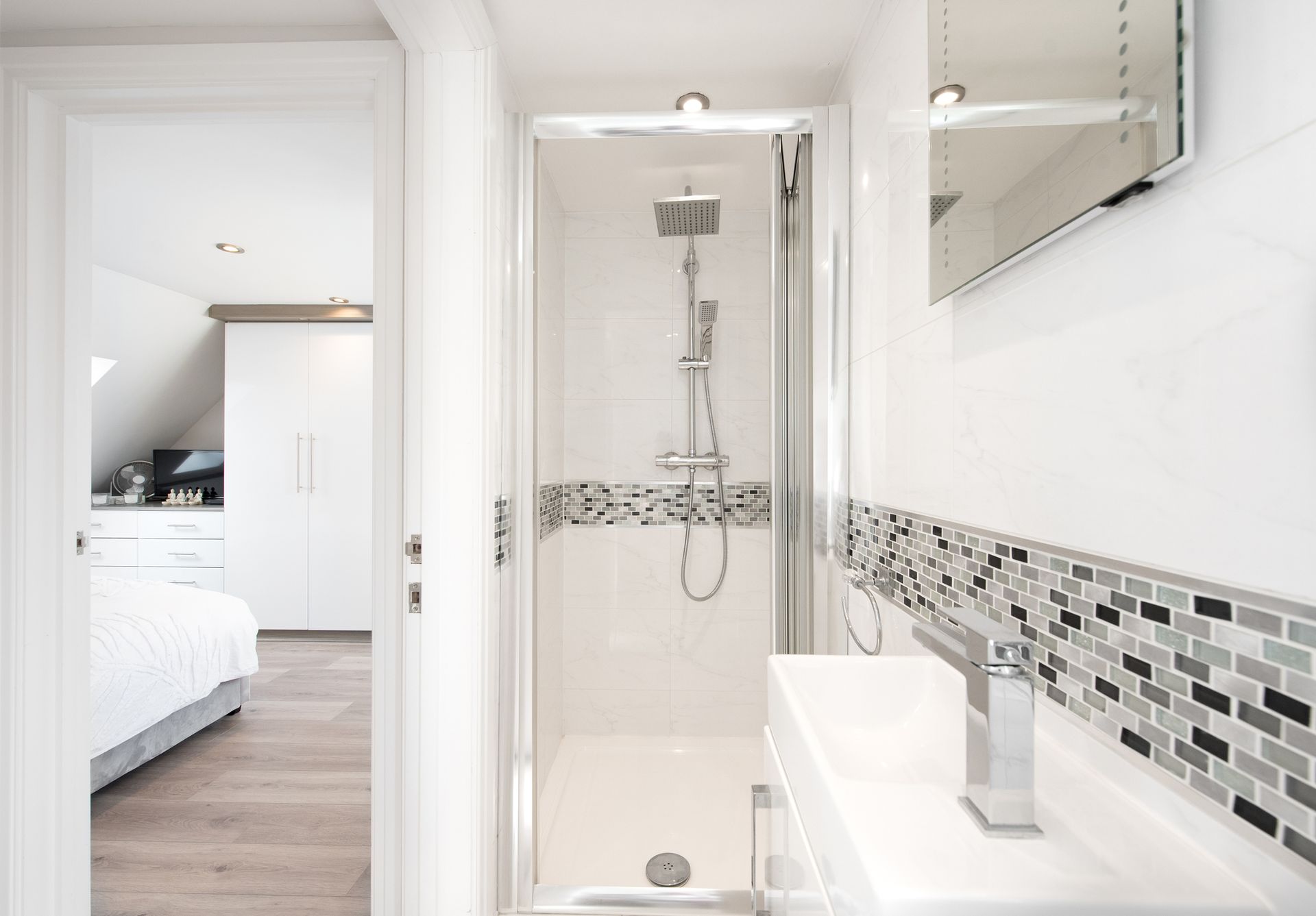 Small white bathroom with a glass-enclosed shower, sink, and an open doorway to a bedroom with closet. Small white bathroom with a glass-enclosed shower, sink, and an open doorway to a bedroom with closet.