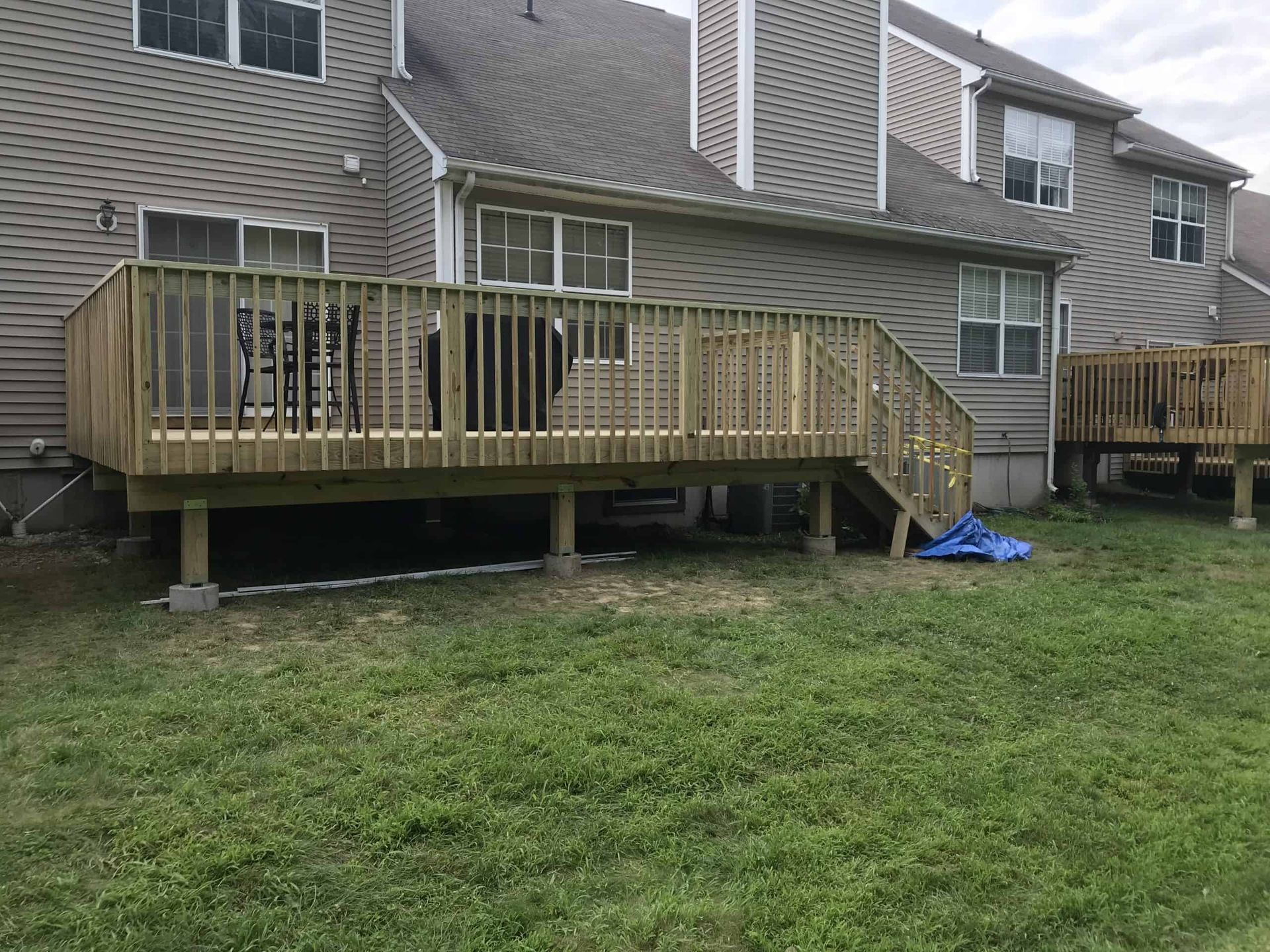 A wooden deck attached to a gray house, with stairs leading down to a grassy yard.