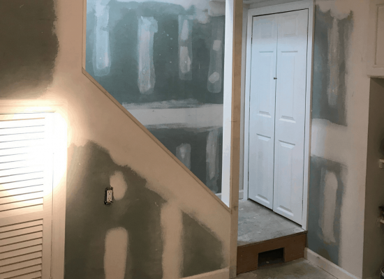 Interior with staircase under construction, featuring drywall and a closed white door.
