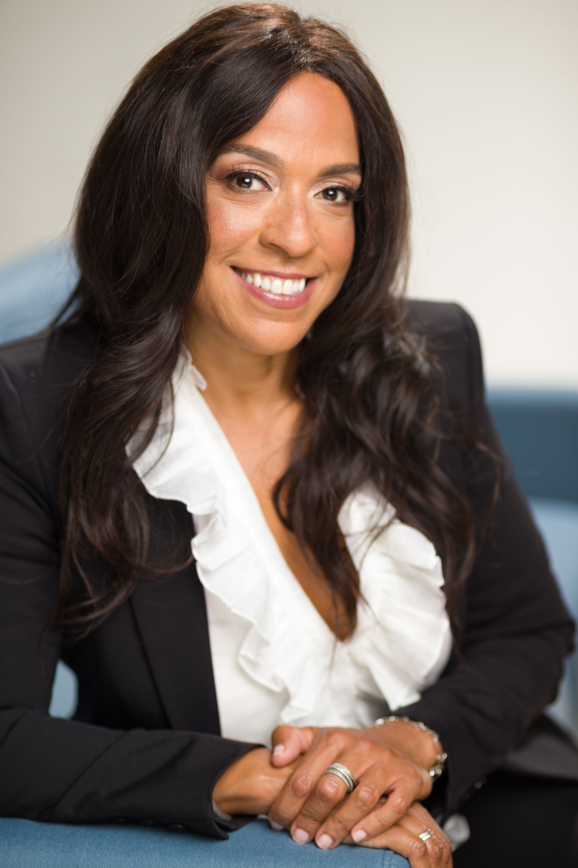 Smiling professional woman in a black blazer and white blouse, seated with hands folded.