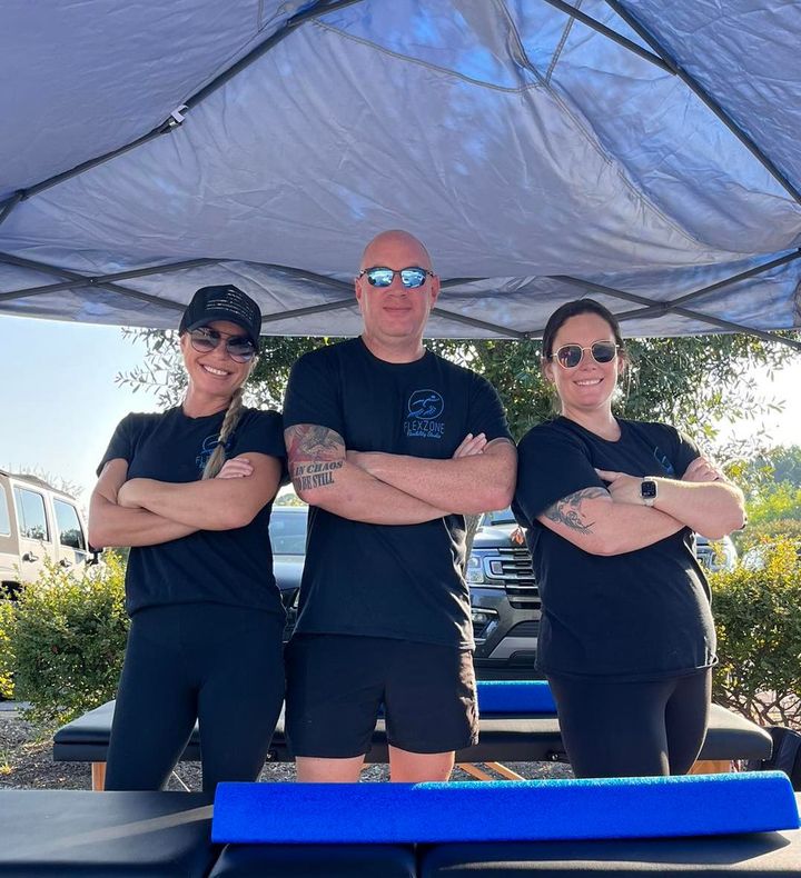 Three people are standing under a tent with their arms crossed.