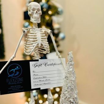 A skeleton is holding a gift certificate in front of a christmas tree.