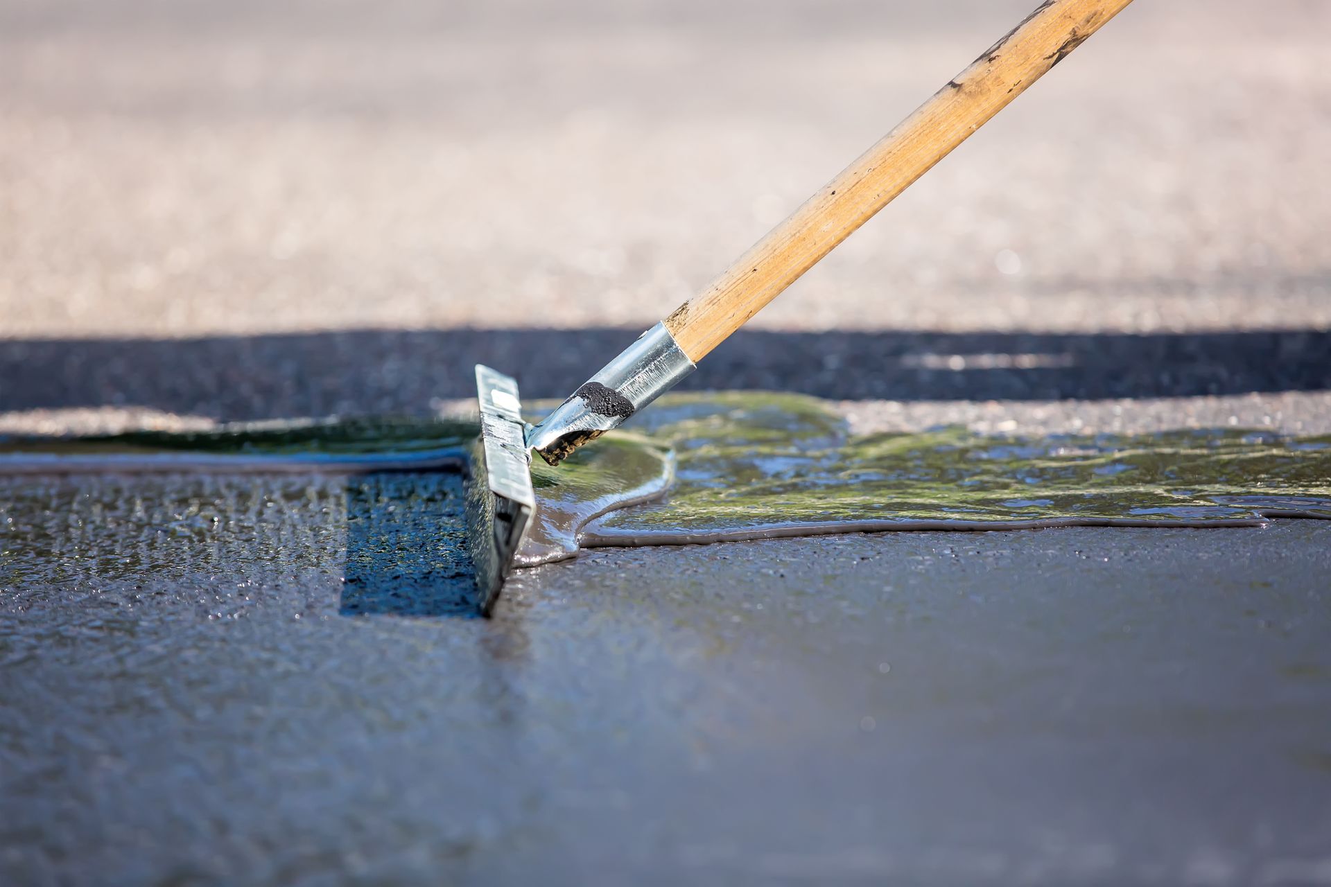Worker applying sealant with squeegee during blacktop asphalt repair on pavement surface. 