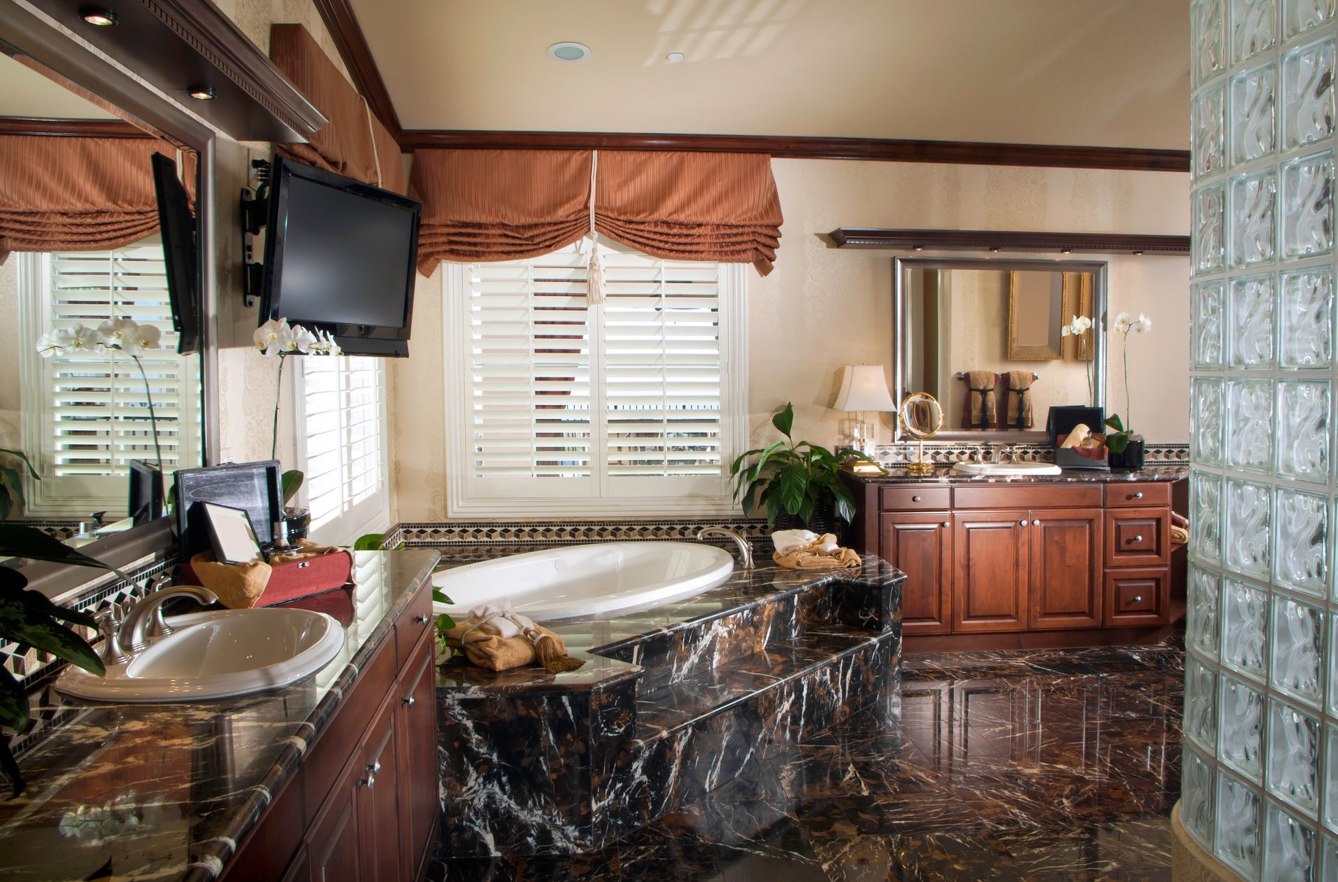 Luxurious bathroom with dark granite countertops, soaking tub, and television.