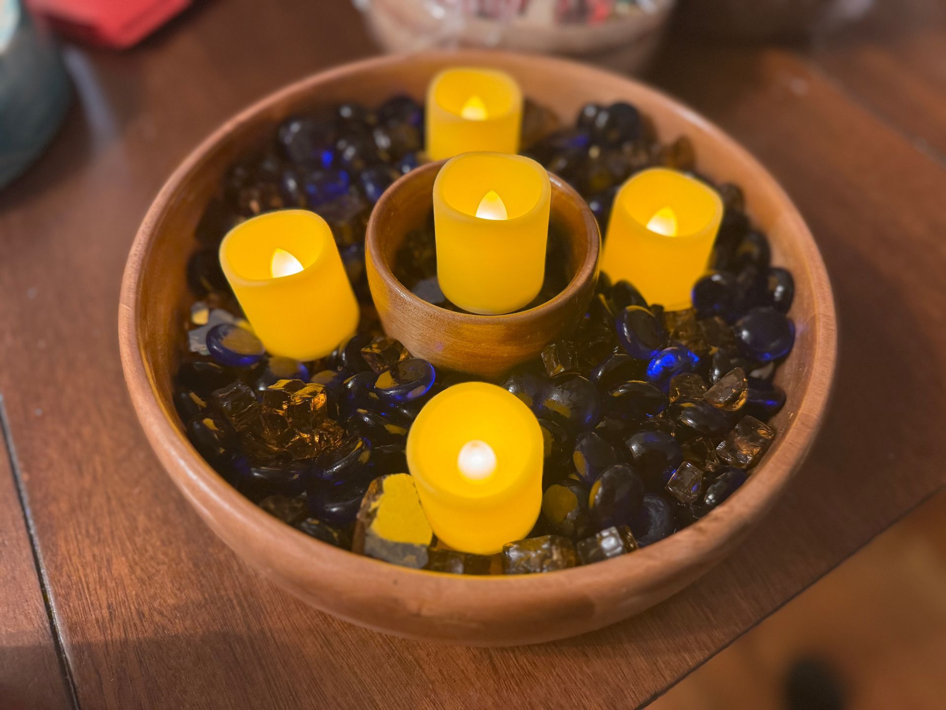 Wooden bowl centerpiece with yellow LED candles surrounded by blue and black glass beads.