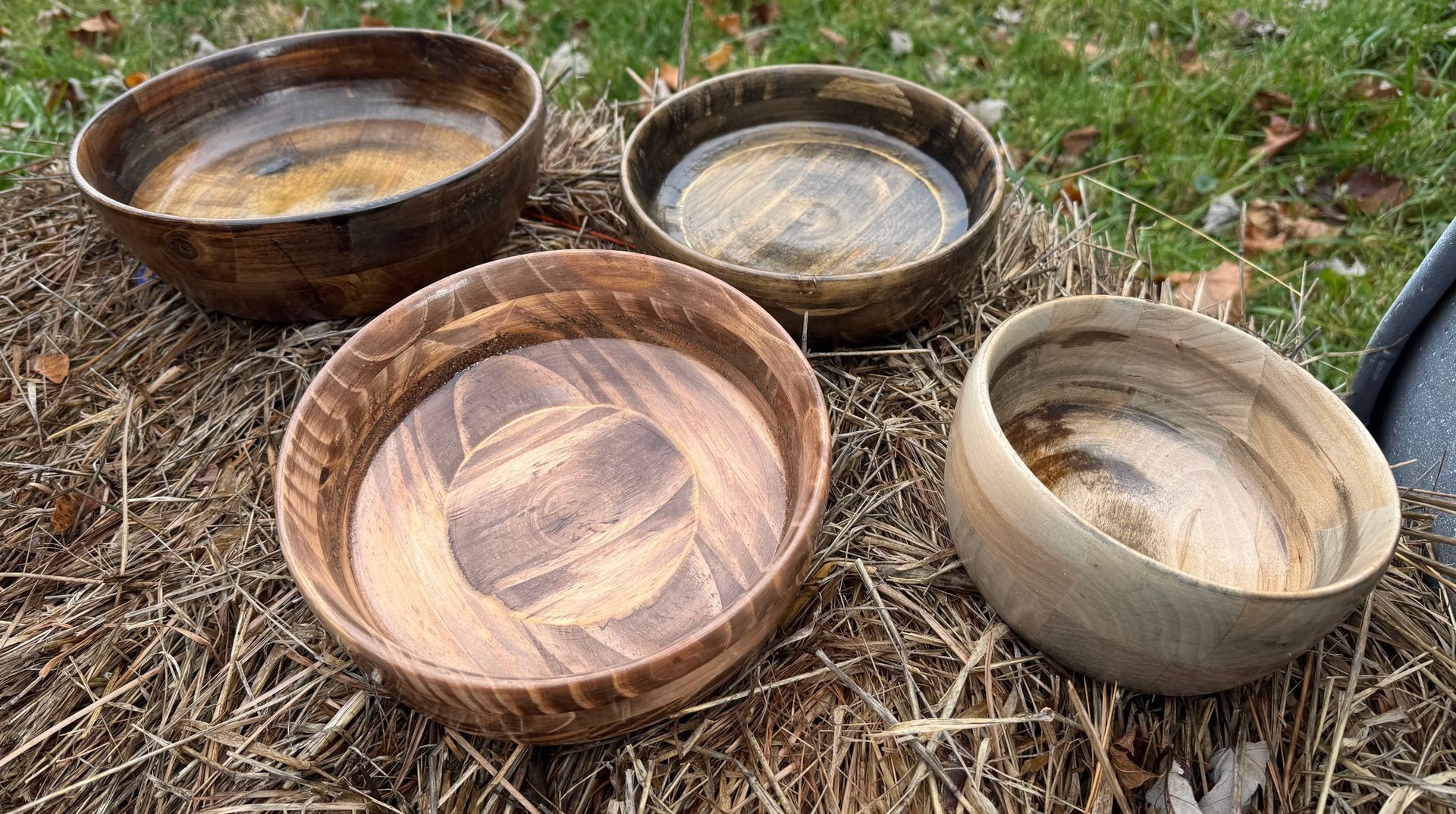 Four wooden bowls with varied wood grain patterns sit on a bed of dry grass.