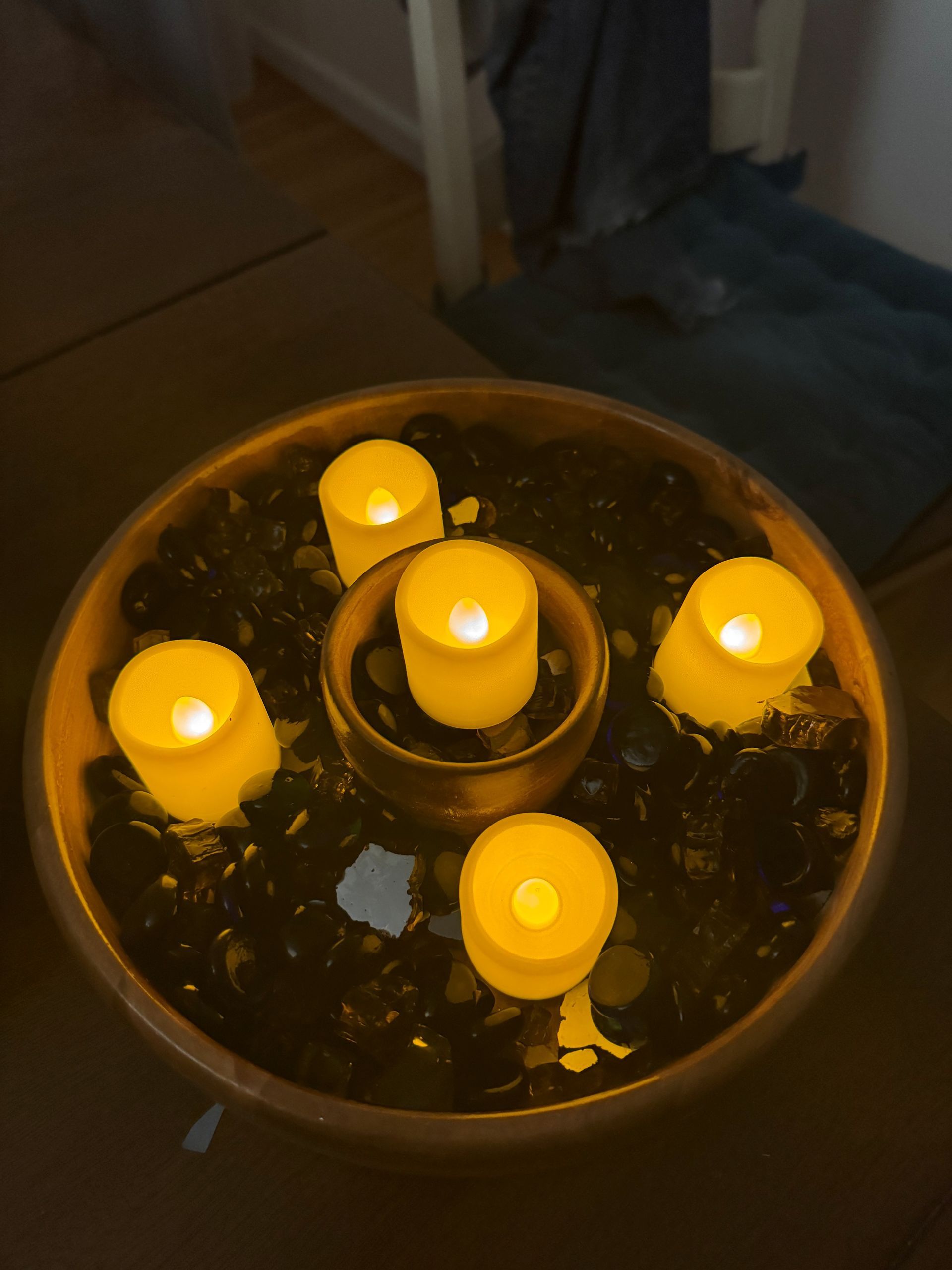 Five lit LED candles in a bronze bowl filled with black rocks.