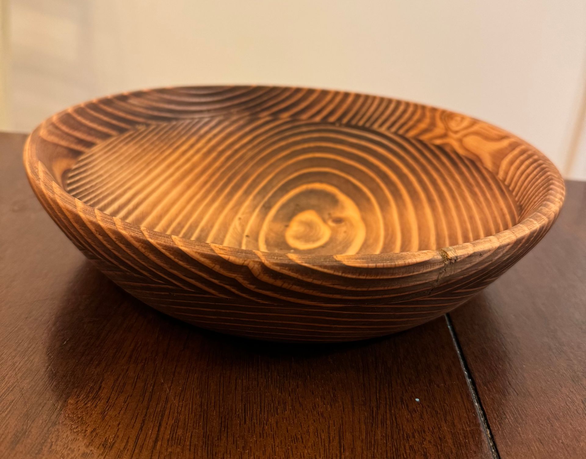 Wooden bowl with concentric grain patterns, shades of brown and tan, resting on a dark wood surface.