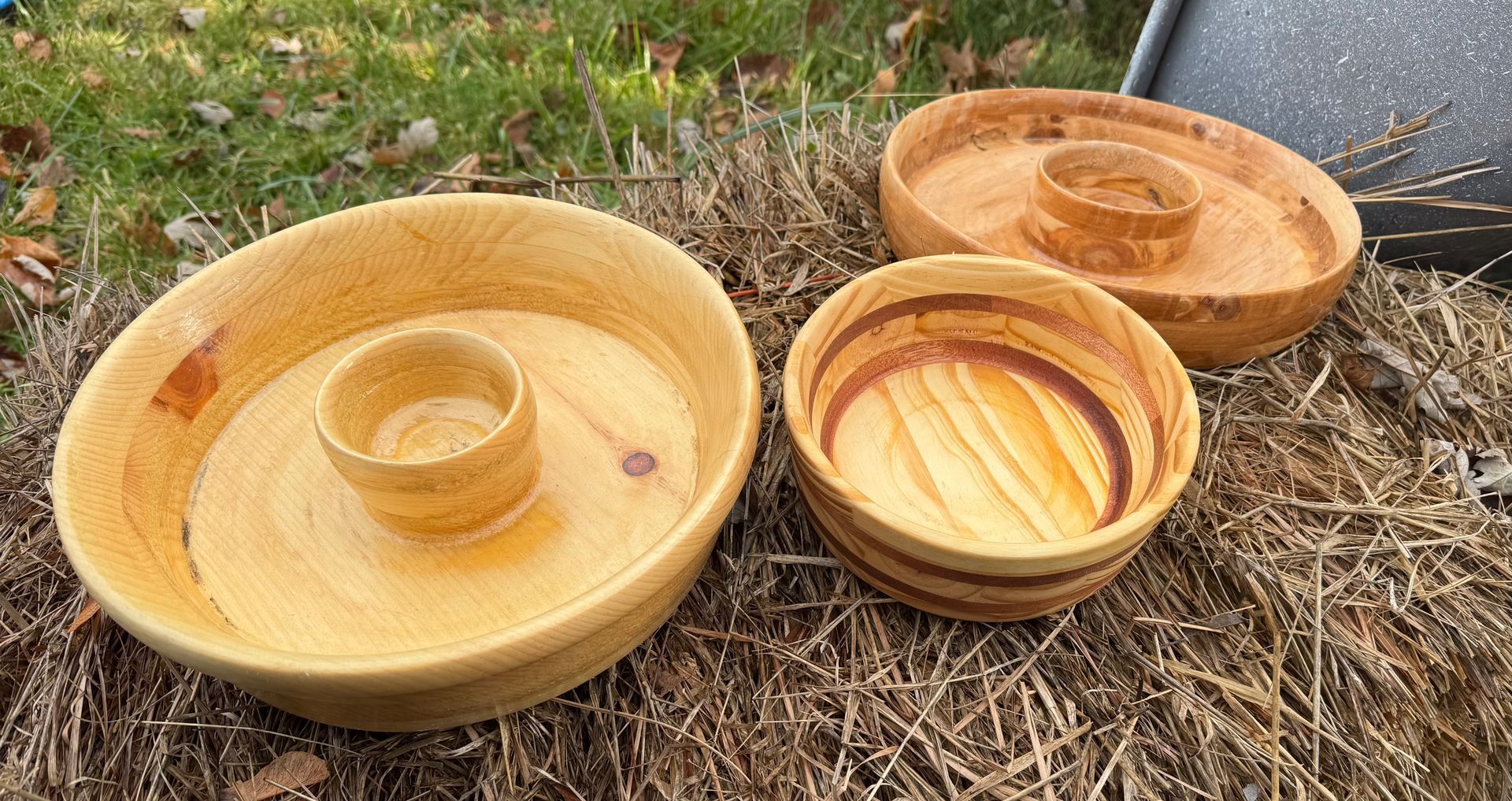 Three wooden bowls of varying sizes with central, smaller bowls, sitting on straw.