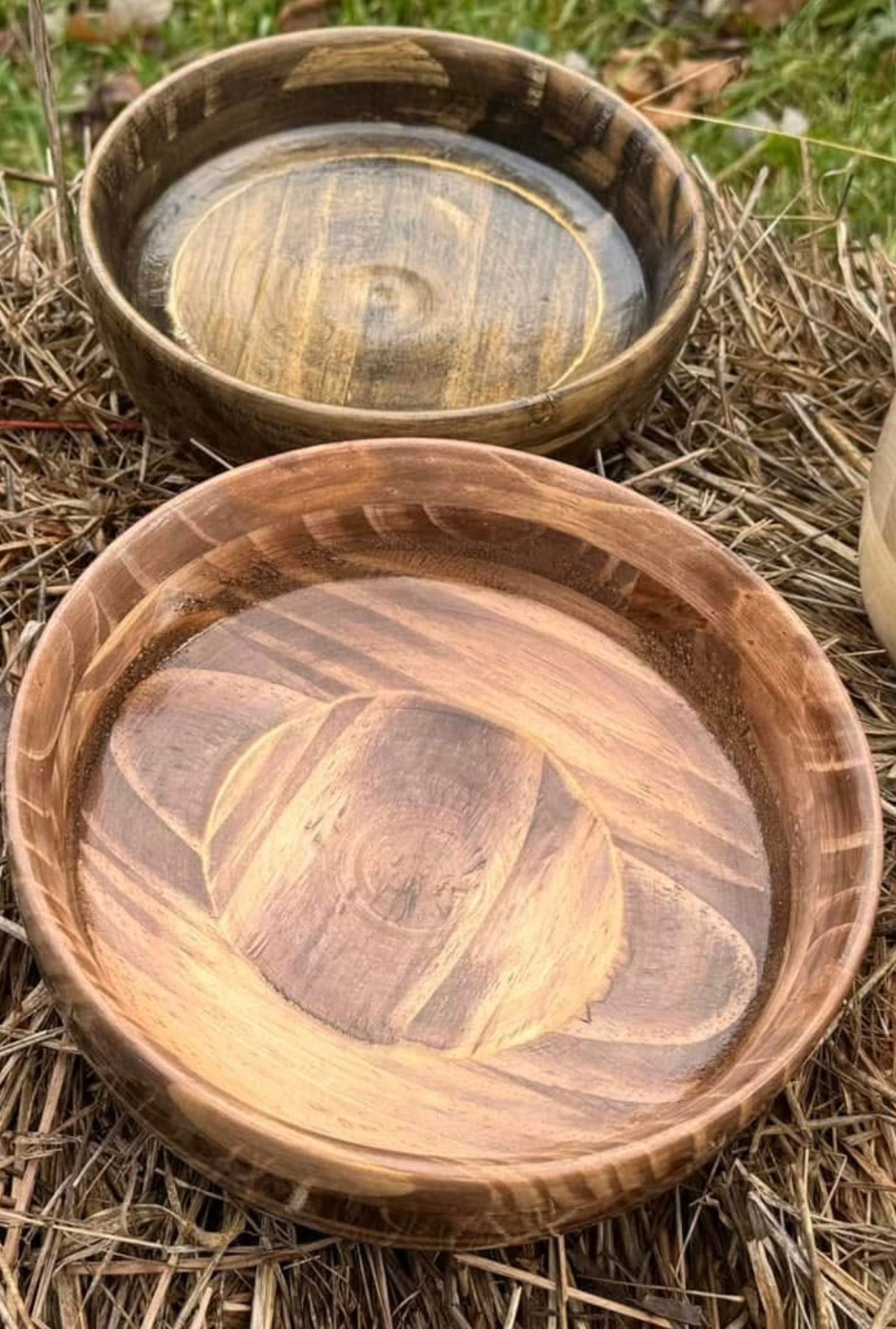 Two wooden bowls with rich wood grain on straw.