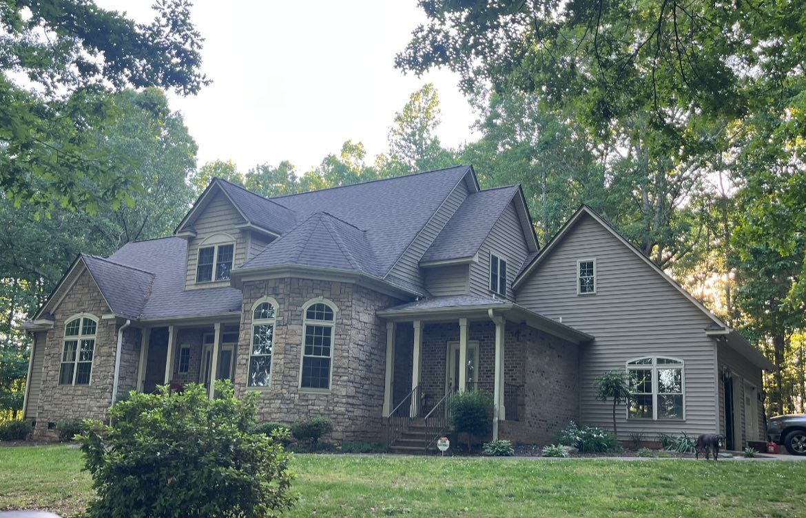 A large house with a blue roof is surrounded by trees and grass.