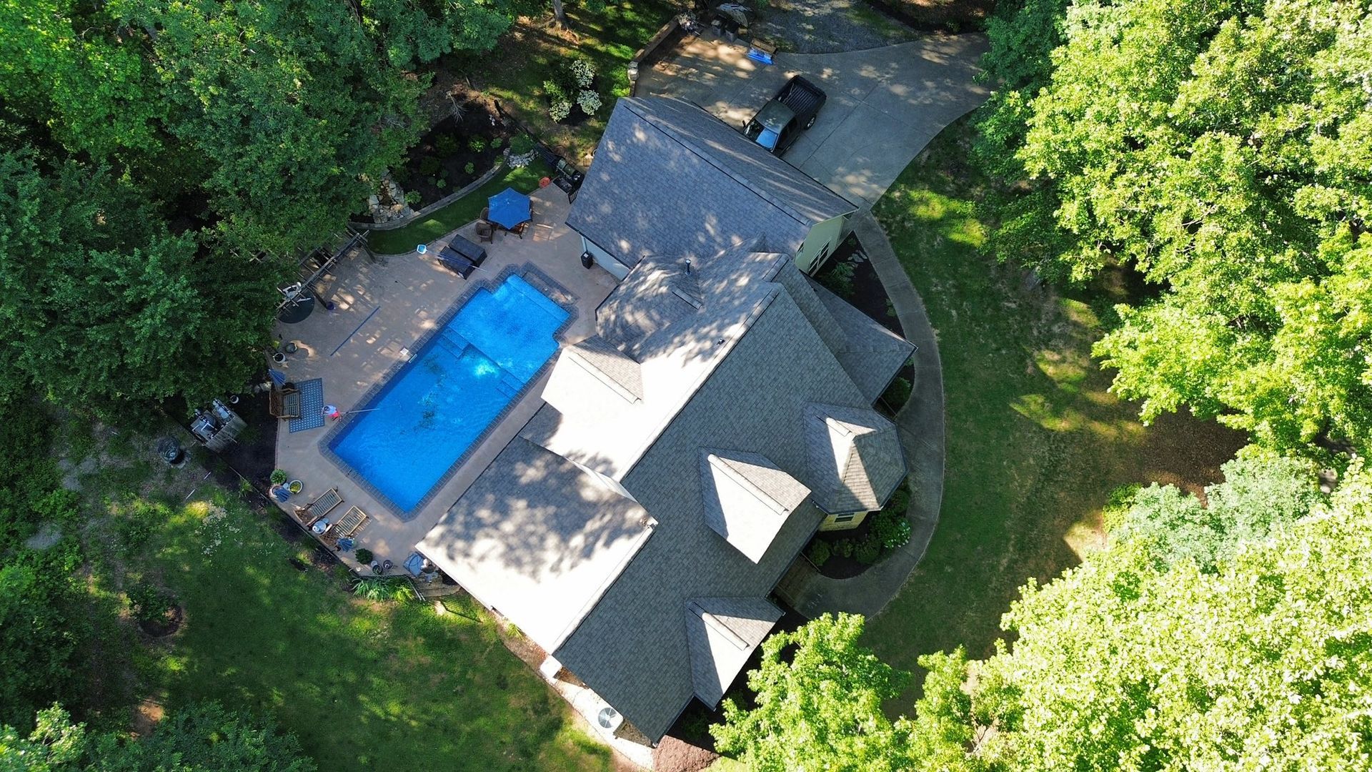 An aerial view of a house with a pool in the backyard surrounded by trees.