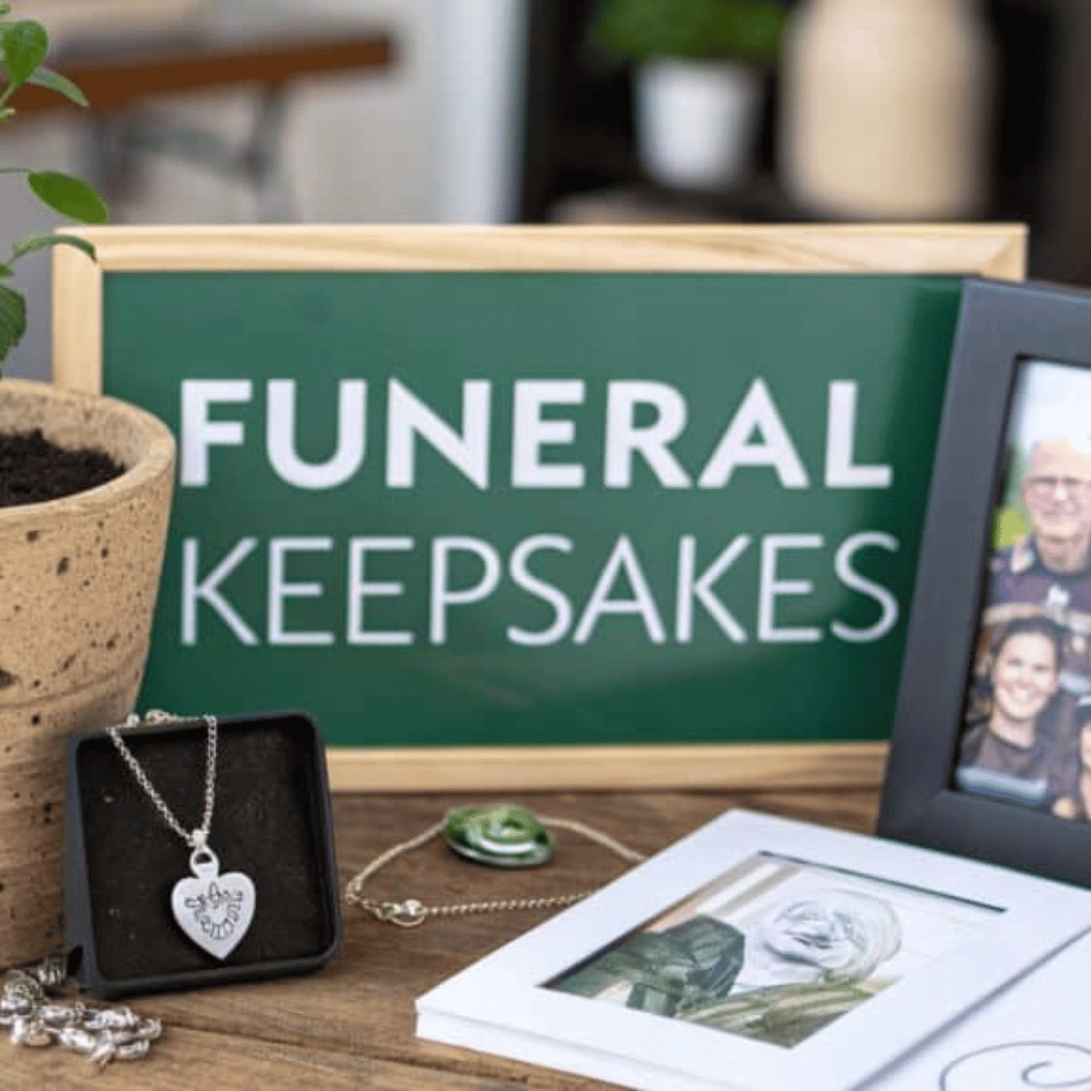 Funeral keepsakes display with pendant, framed photo, and green sign on a wooden table