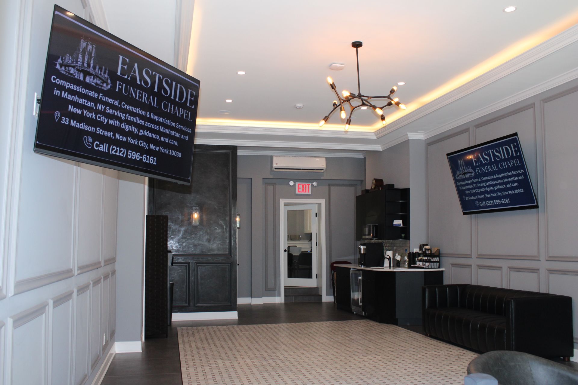 Elegant hotel lobby with chandeliers, wall-mounted TVs, and a reception desk near the entrance