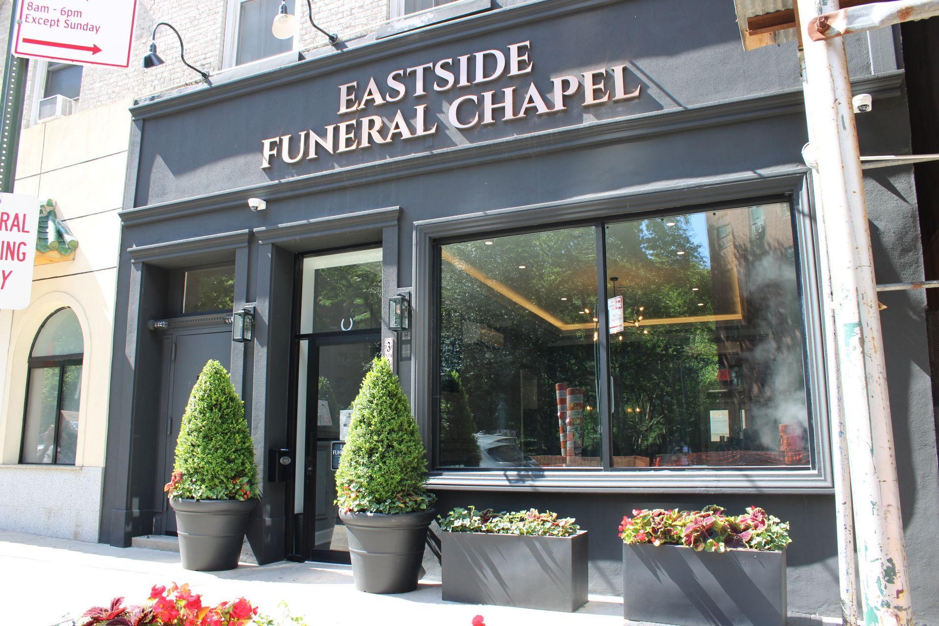 Eastside Funeral Chapel storefront with black sign, glass windows, and potted shrubs on the sidewalk