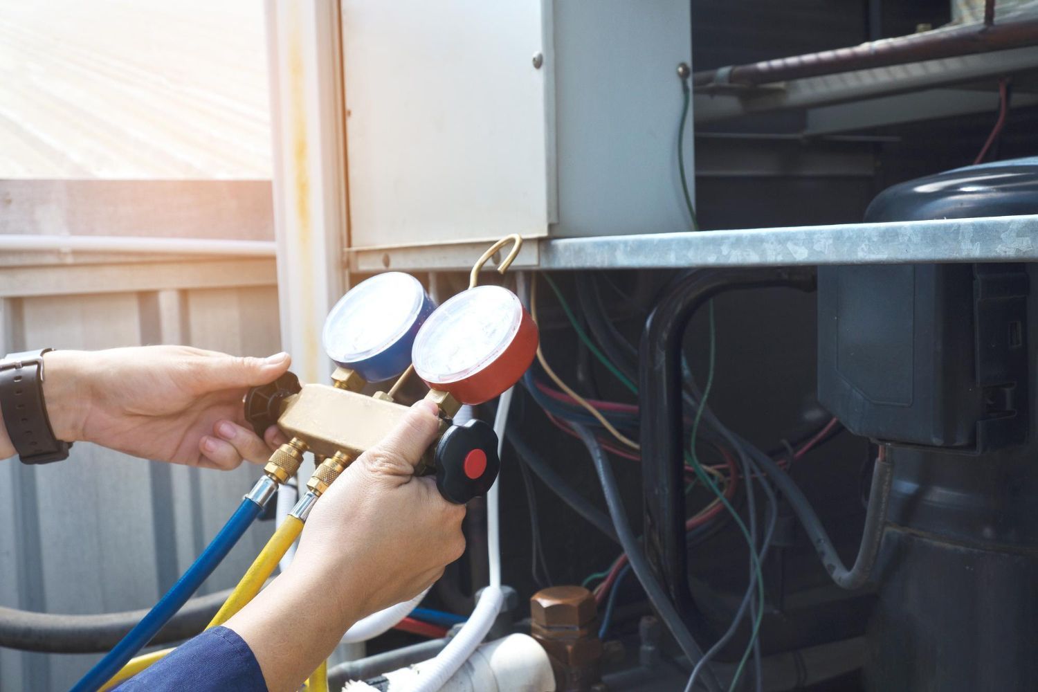 Technician connecting gauges and hoses to outdoor HVAC unit for service