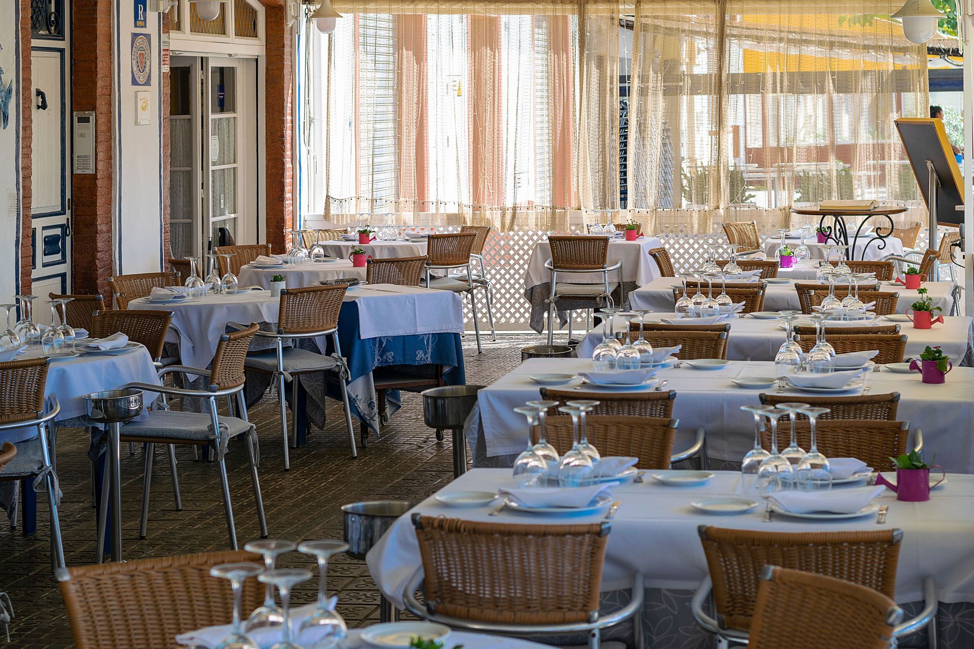 Outdoor restaurant patio with tables set with white tablecloths and wicker chairs under warm evening light