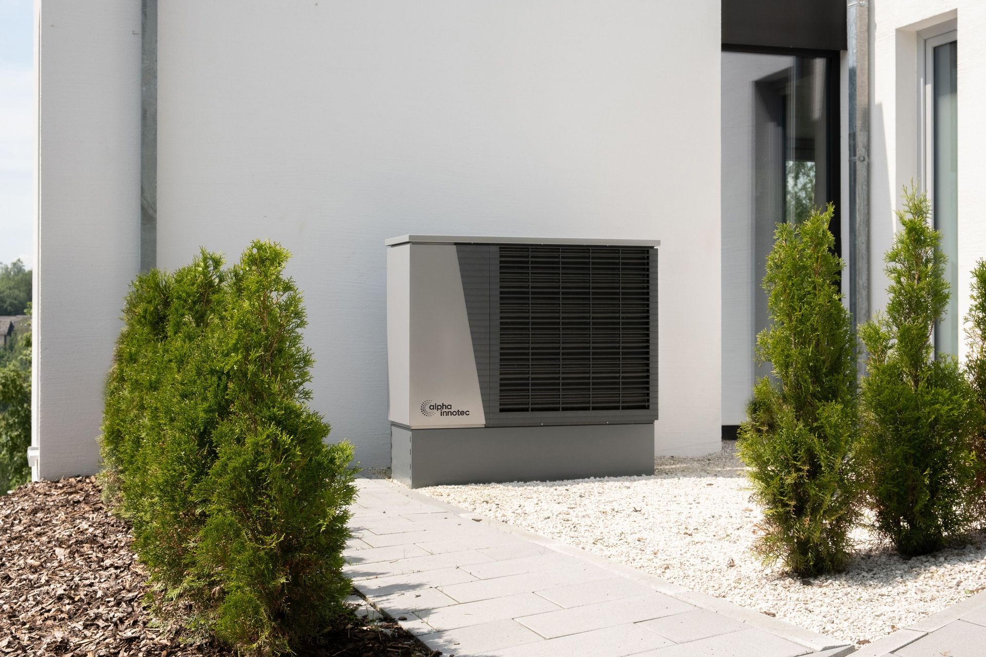 Outdoor HVAC unit beside a white building, framed by green shrubs and gravel.