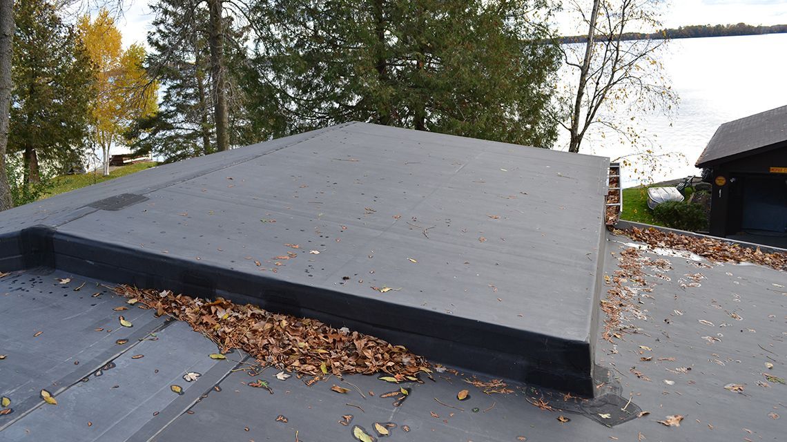 A flat, black roof covered in brown leaves