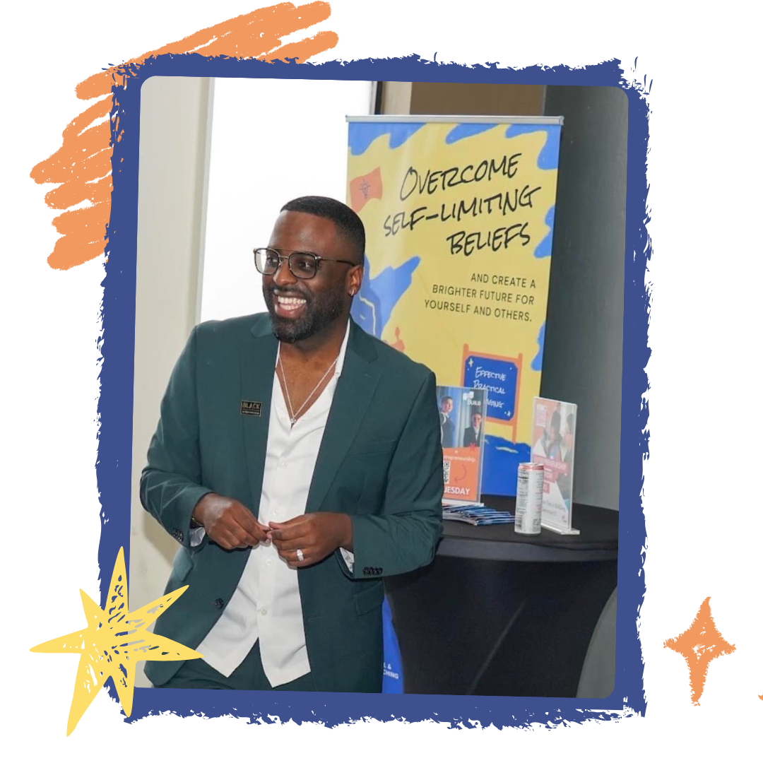 Tony Shavers III in green suit smiles at a table with a banner that says