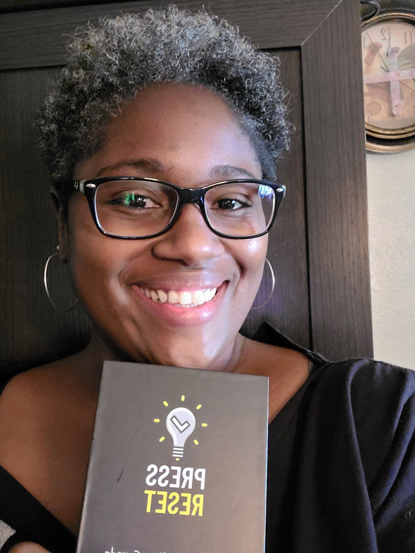 A beautiful woman with a short afro, smiling and holding her new Press Reset card deck.