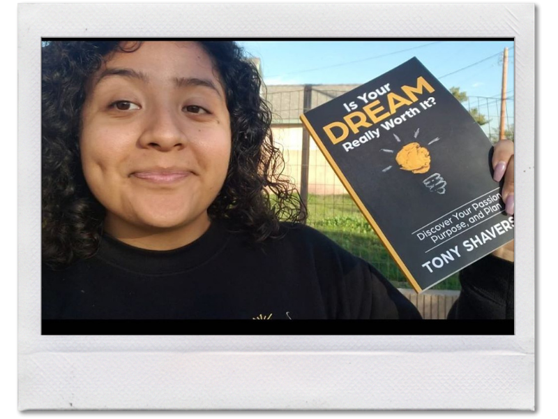 Smiling female entrepreneur holding Tony Shavers III's self help book - Is Your Dream Really Worth It?