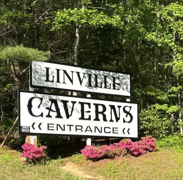 Sign for Linville Caverns, white letters on black background, with red flowers in front.