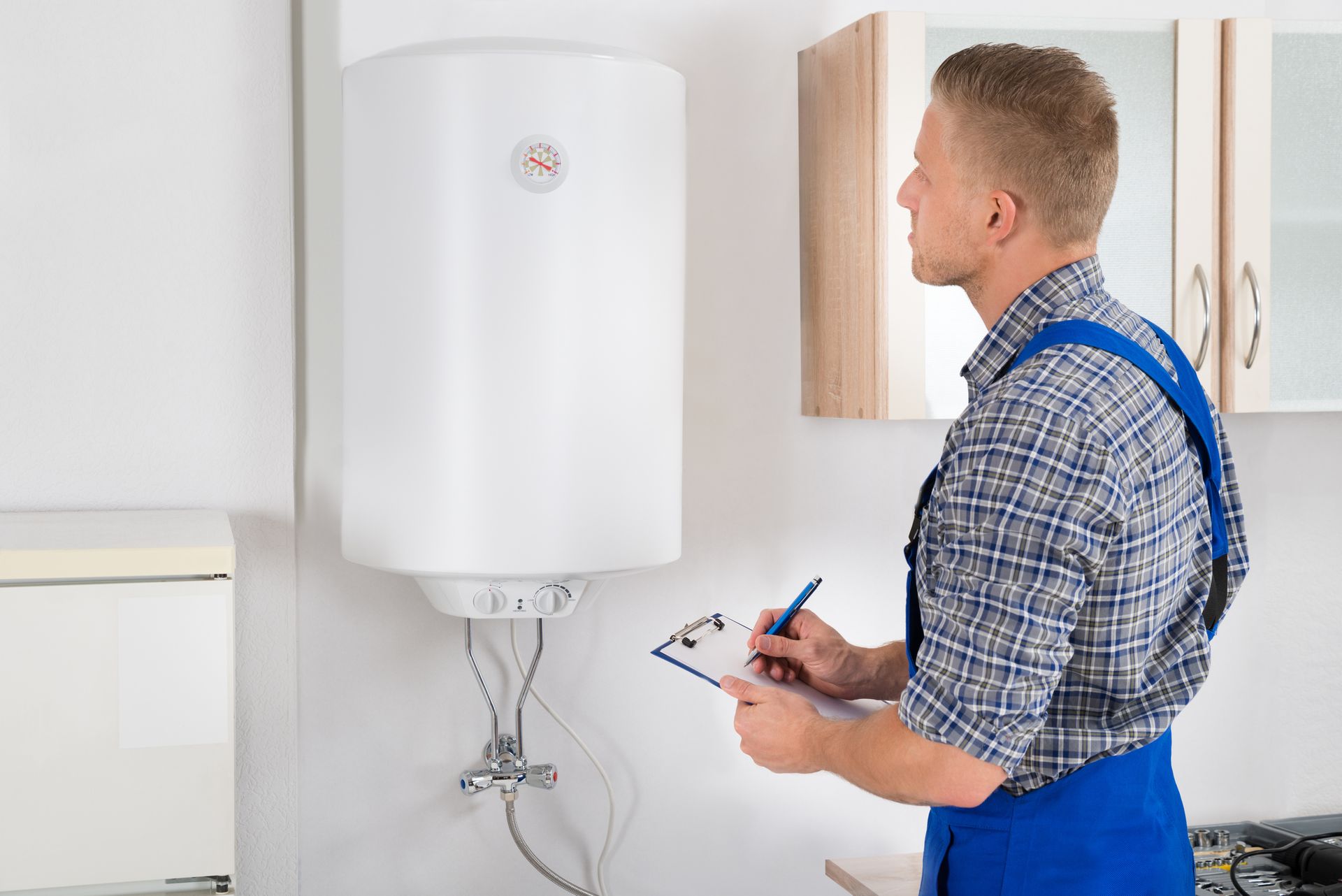 A man is writing on a clipboard in front of a water heater.