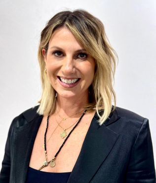 A woman wearing a black jacket and a necklace is smiling for the camera.
