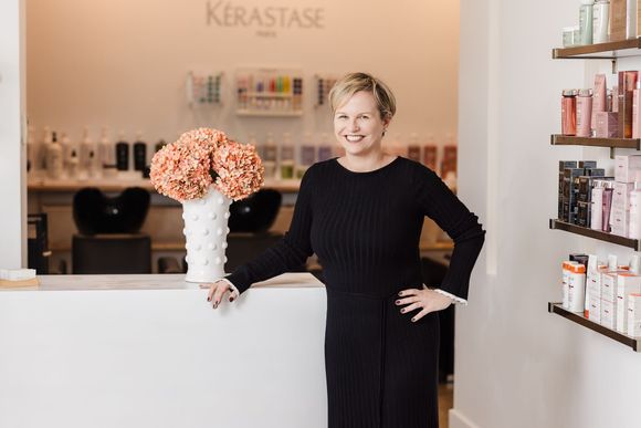 A woman is standing behind a counter in a hair salon holding a vase of flowers.