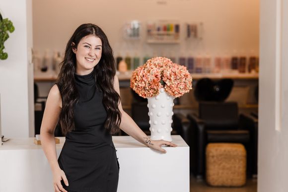 A woman in a black dress is standing in a salon next to a vase of flowers.