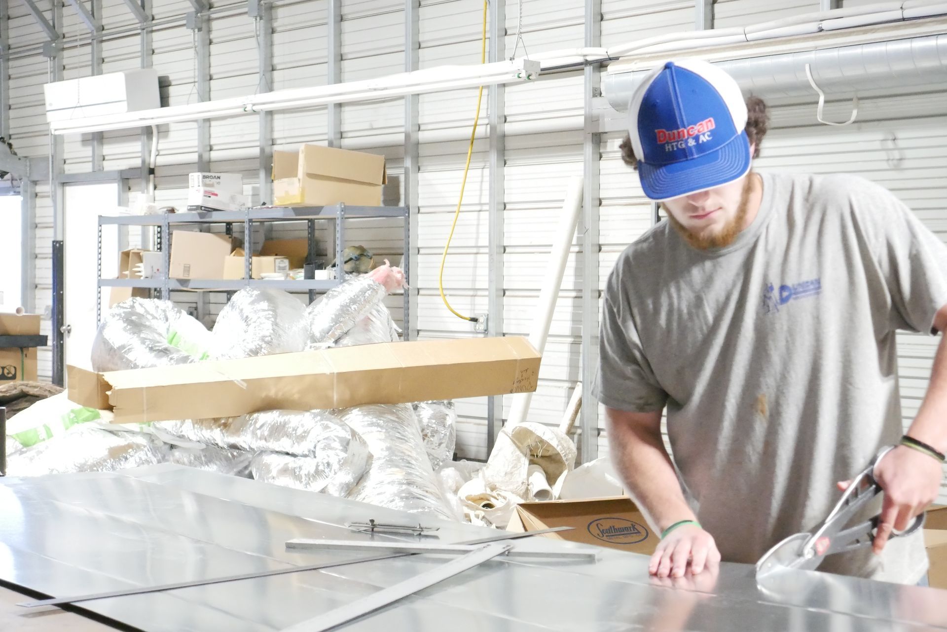 A man in a blue hat is working on a piece of metal in a factory.