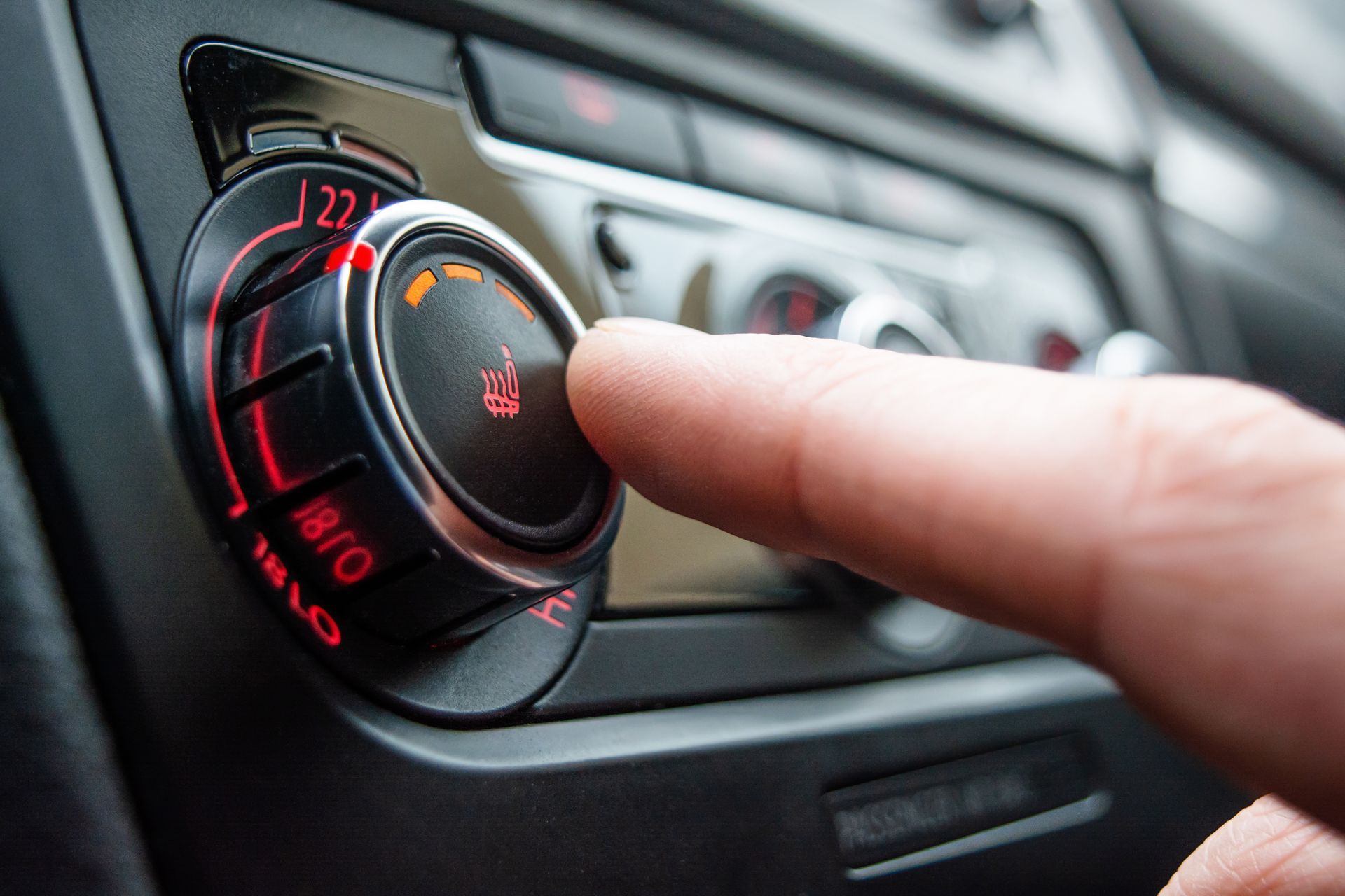 Hand turning a car's climate control dial, with a red illuminated setting.