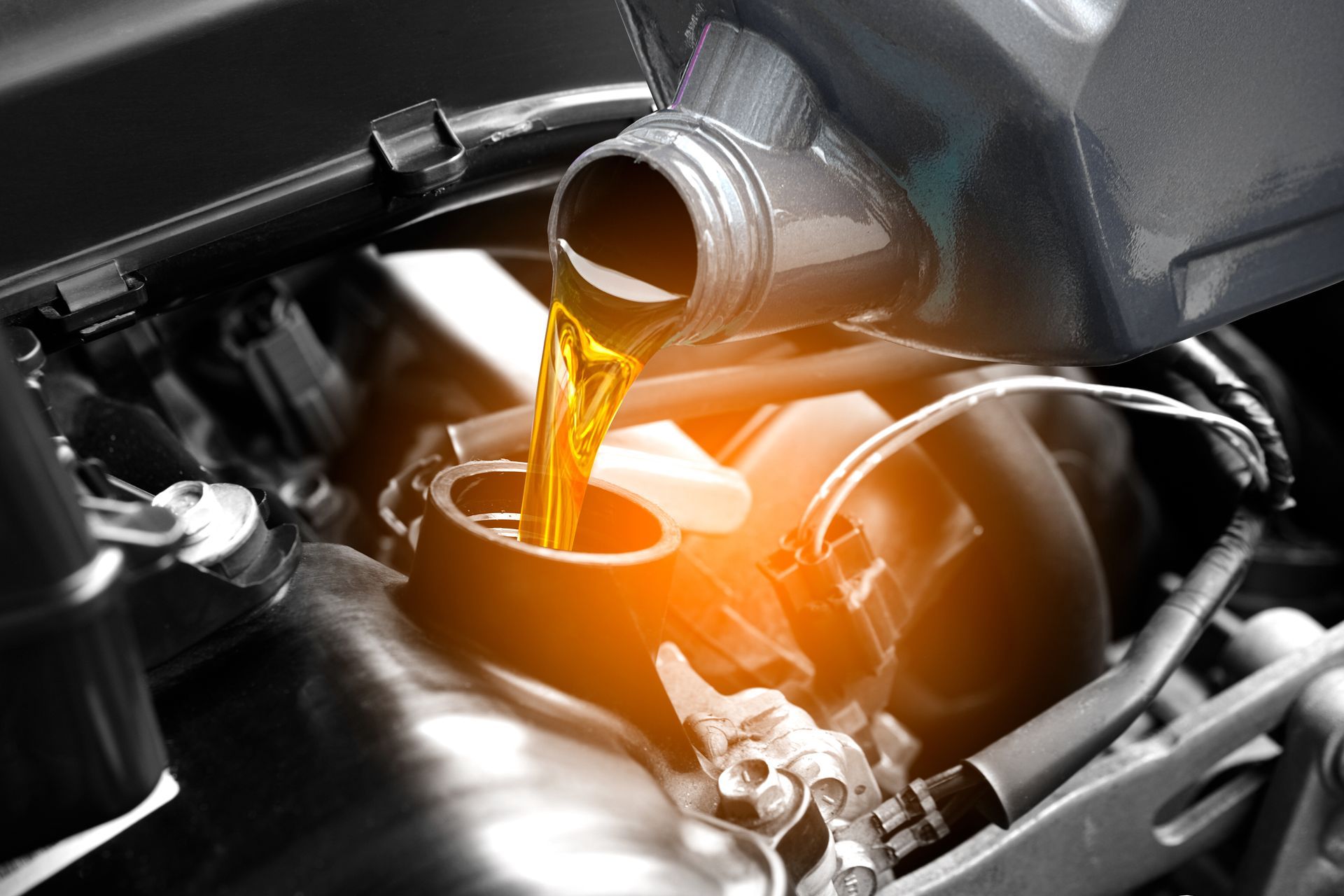 Pouring oil into a car engine. Yellow oil from a gray container fills the engine compartment.