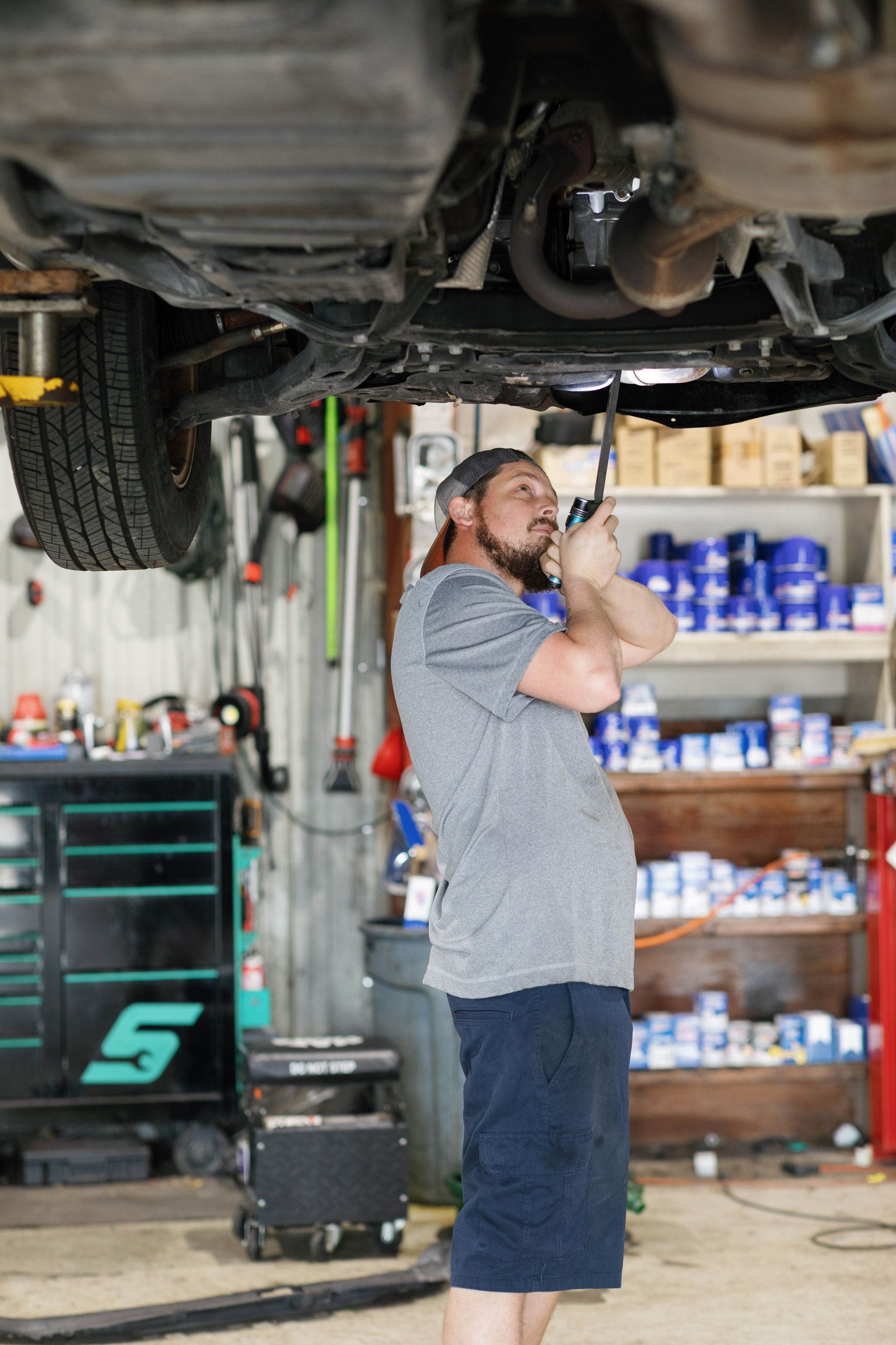 Mechanic working under a car on a lift in a garage, using a tool.