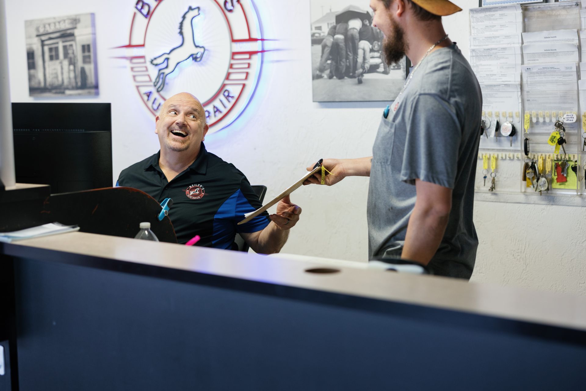 Man at a counter smiles, receives keys from another man in auto repair shop.