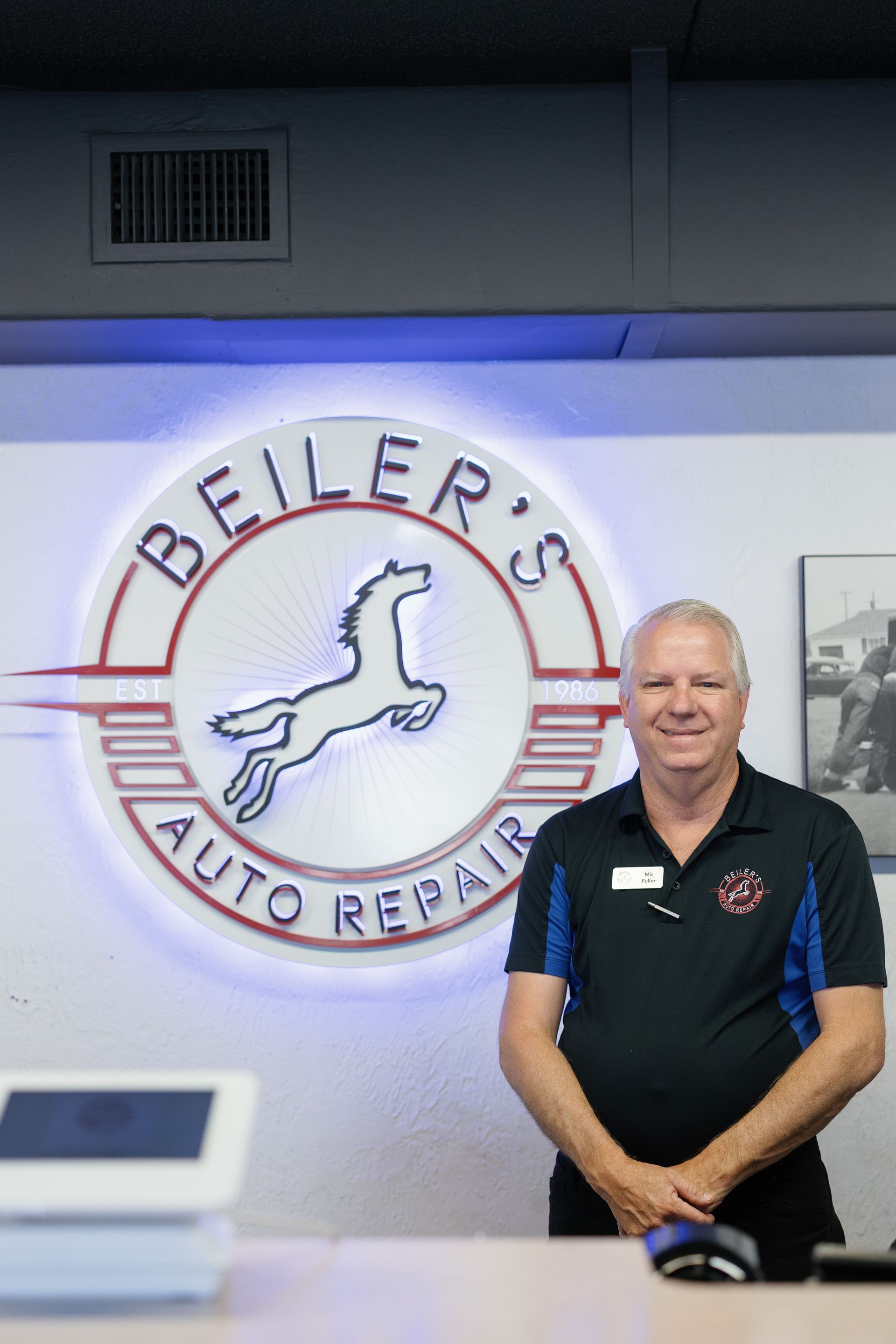 Man standing in front of a neon sign for Beiler's Auto Repair.