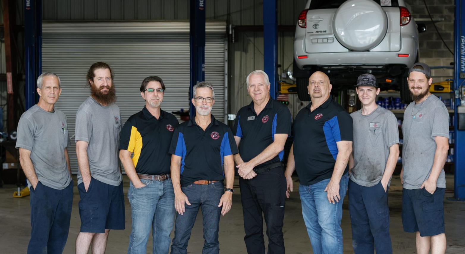 Group of people standing in a workshop in front of a large vehicle engine and tires