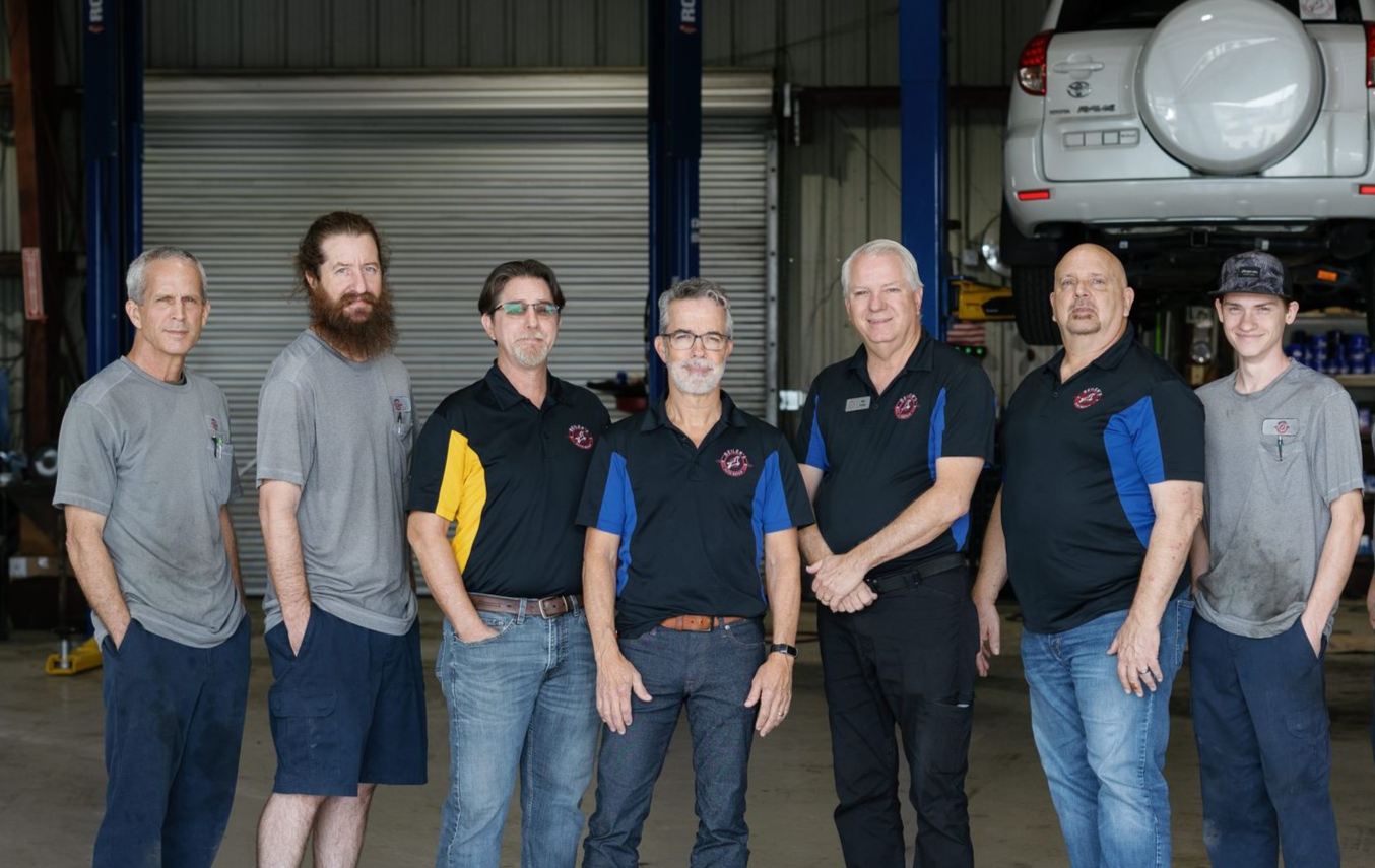 Group of people standing in a workshop in front of a large vehicle engine and tires