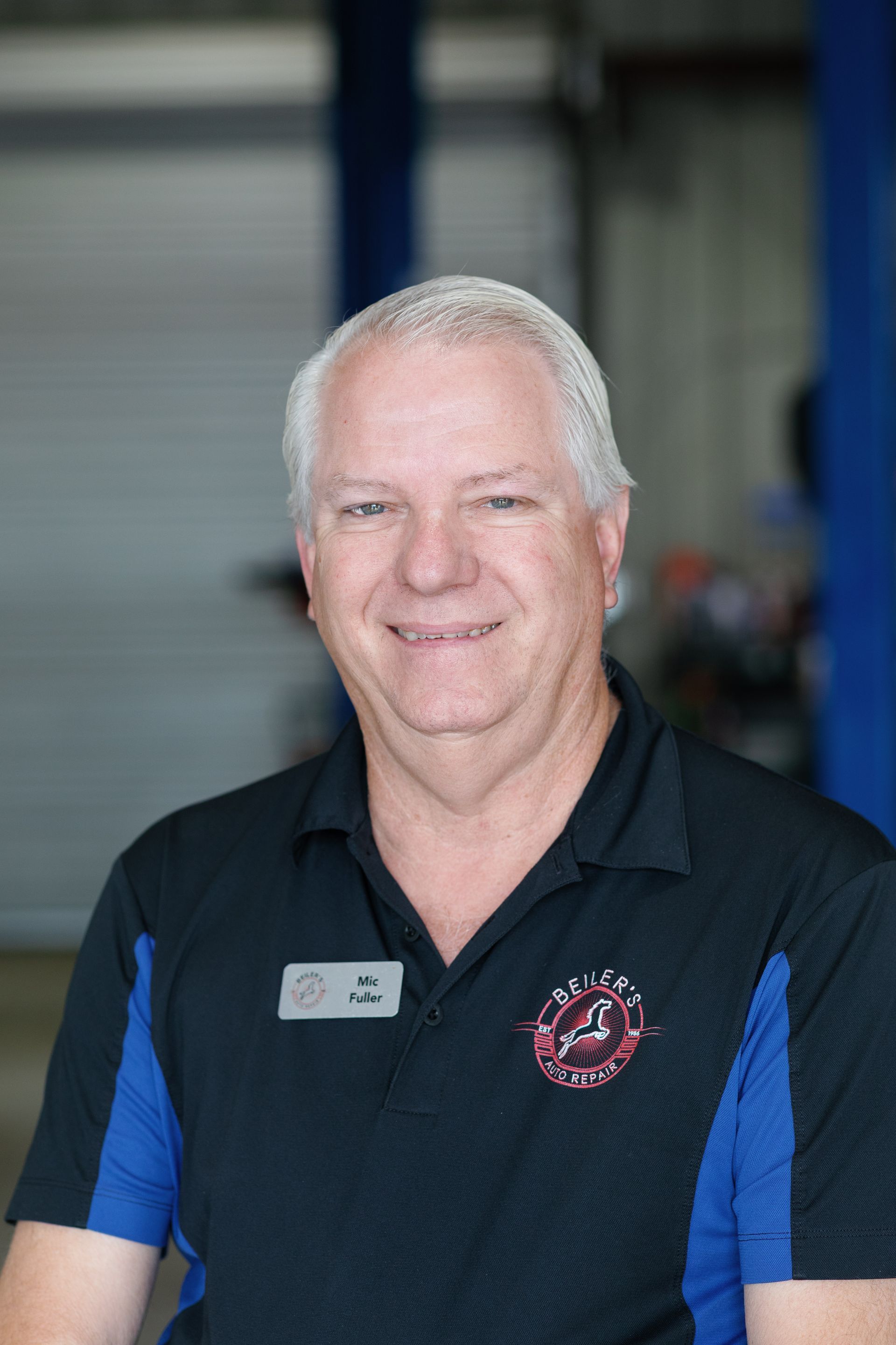 Man in black and blue collared shirt smiling in a garage.