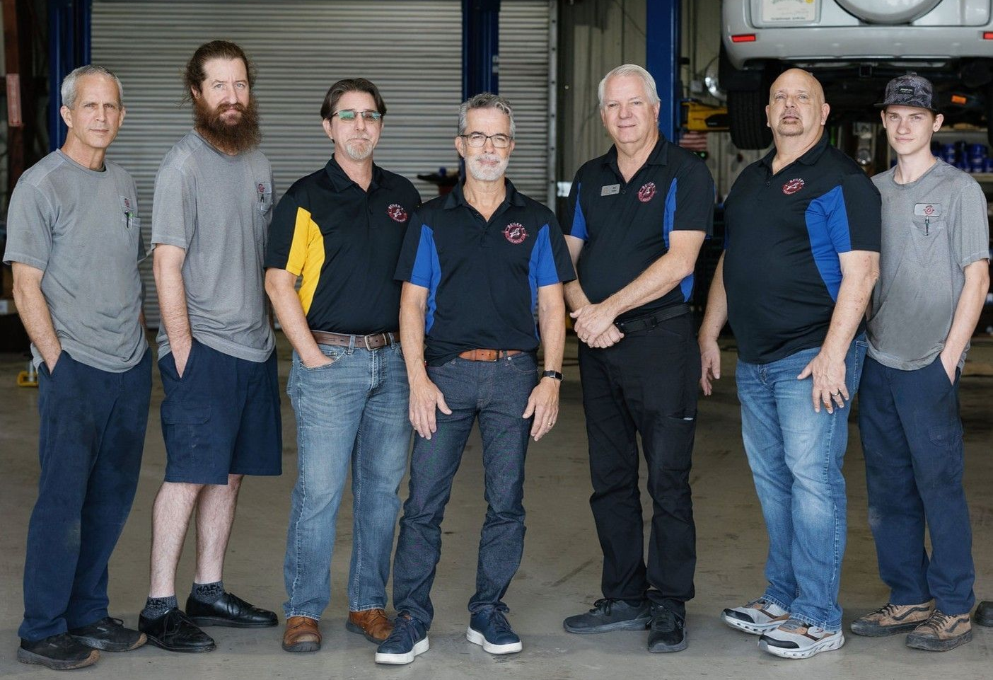 Group of people standing in a workshop in front of a large vehicle engine and tires