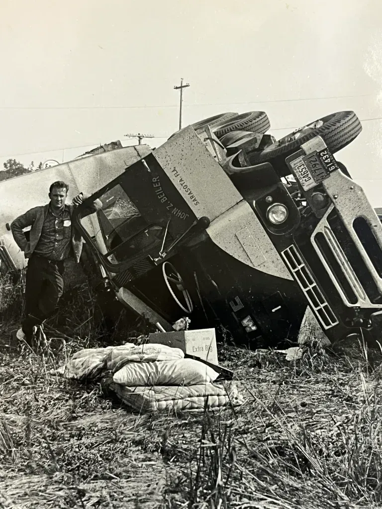 Man standing next to a tipped-over truck on the side of a road.
