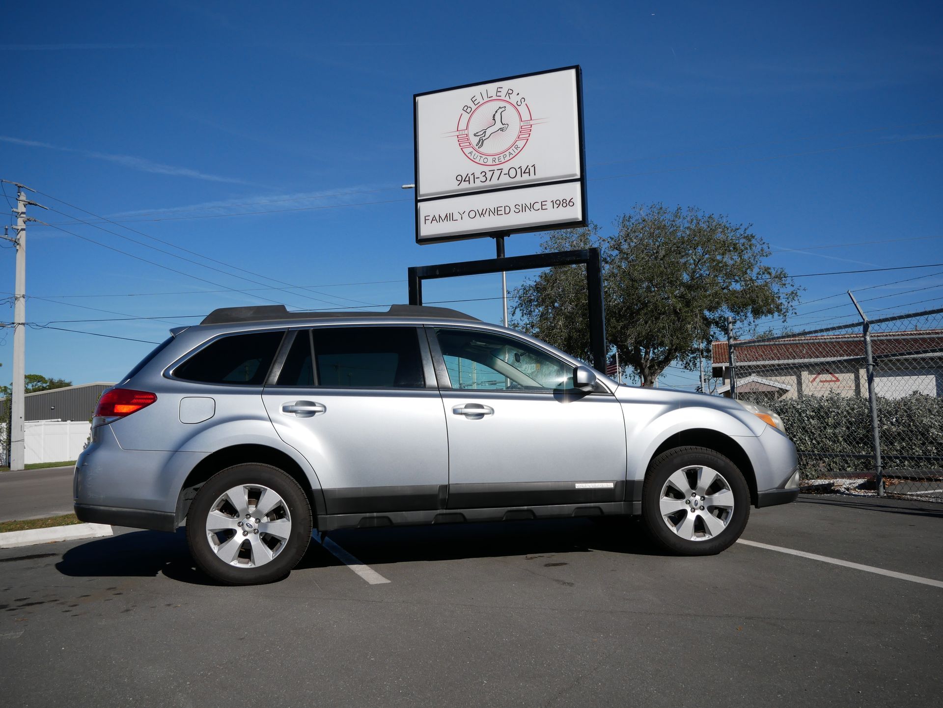 Silver Subaru Outback parked in a lot, with a business sign in the background on a sunny day.