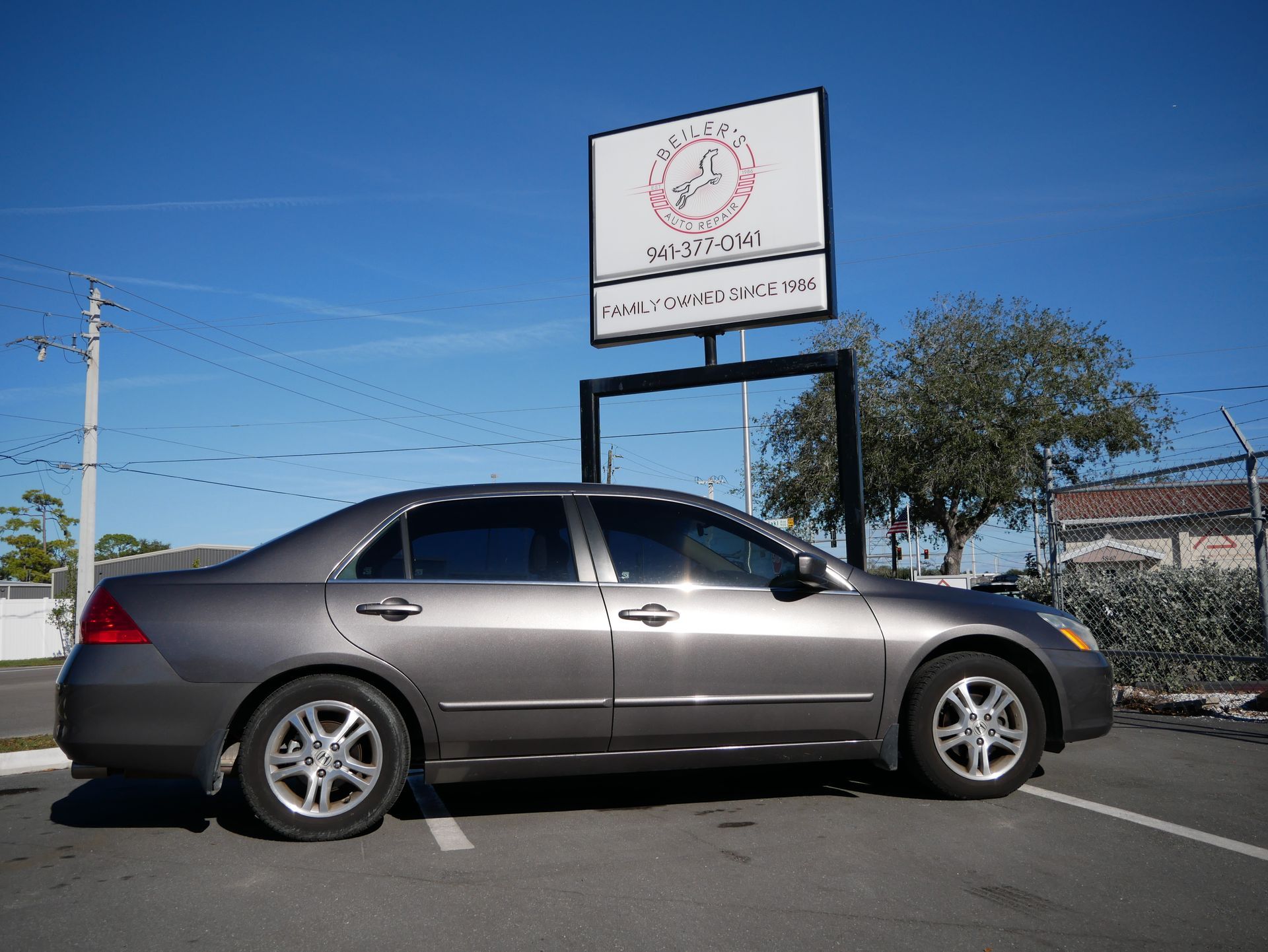 Gray sedan parked in front of a business sign on a sunny day.