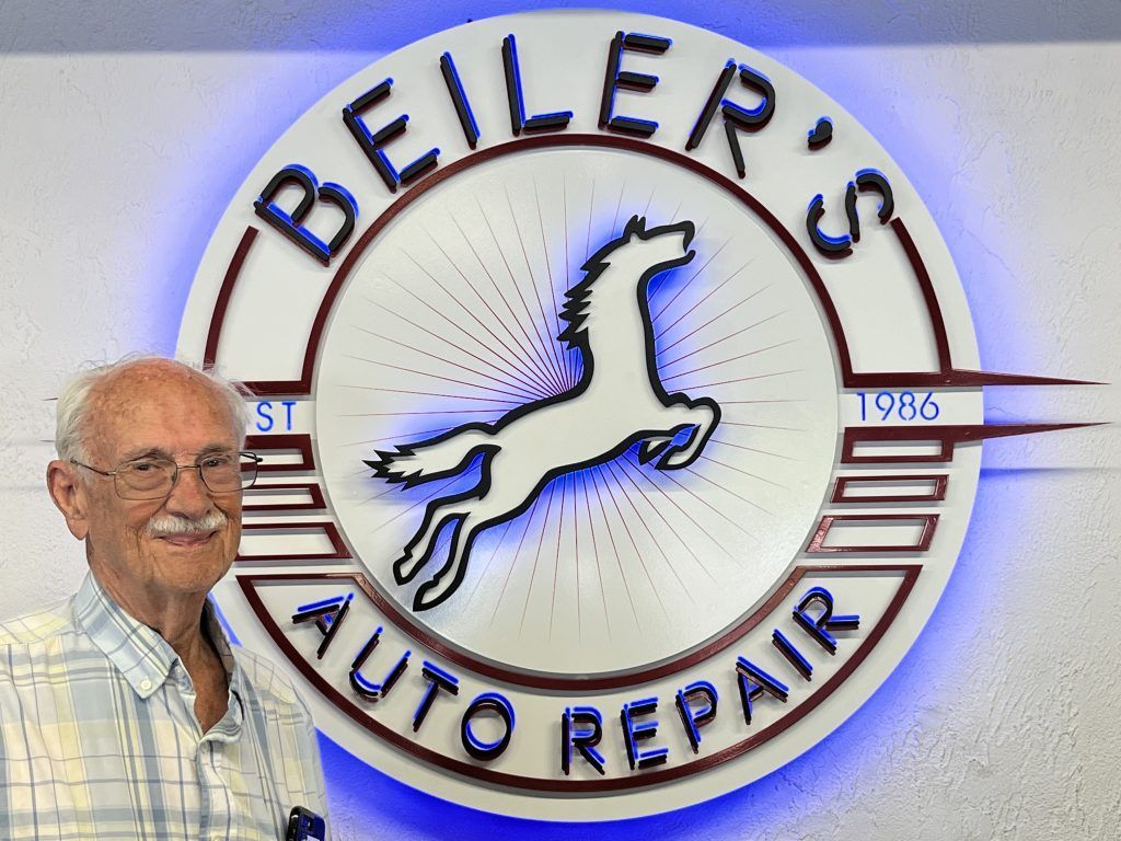 Man standing in front of a sign for Beiler's Auto Repair, featuring a leaping horse logo.