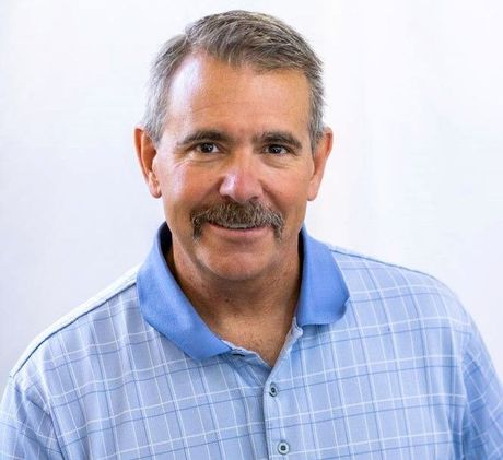 A man with a mustache is wearing a blue plaid shirt and smiling.