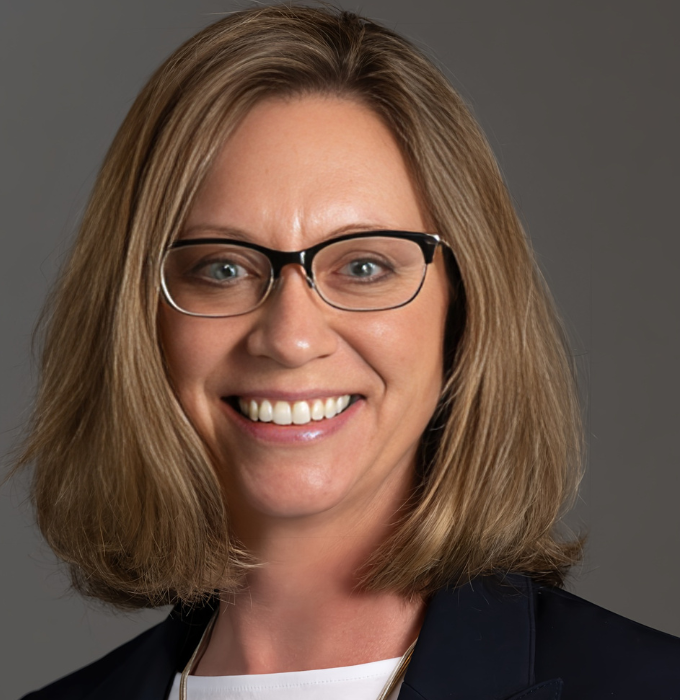 A woman wearing glasses and a suit smiles for the camera