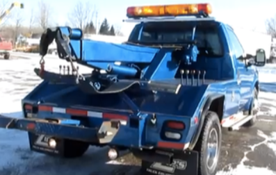 Picture of a parked blue  tow truck. The tow truck is idle and is not towing.